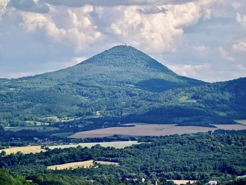 Forested conical hill above patchwork farmland with village below and broad.. Stock Photos