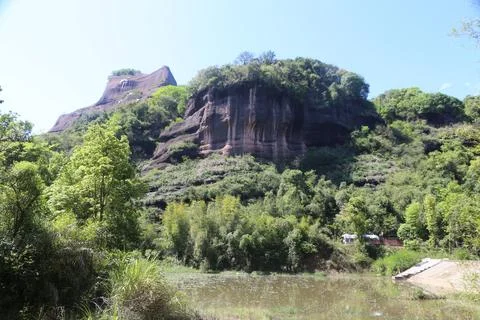 Forested red rock cliffs above a pond in bright daylight Stock Photos