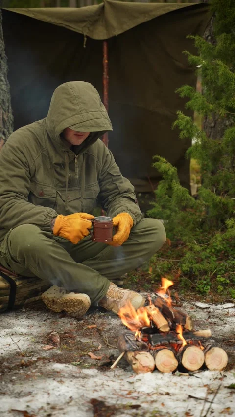 A forester in a coniferous forest is drinking tea, warming himself by the fire Stockbeeldmateriaal 307007919