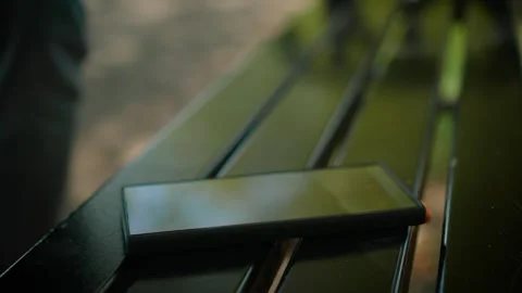 Forgotten mobile phone left on metal bench while stranger taking it and walking Stock Footage 333580357