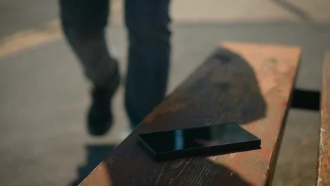Forgotten smartphone on wooden bench while stranger picking it up and walking Stock Footage 334325833