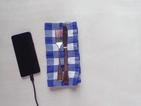 Fork and kinife table setting on a blue and white gingham napkin with a cellp Stock Photos