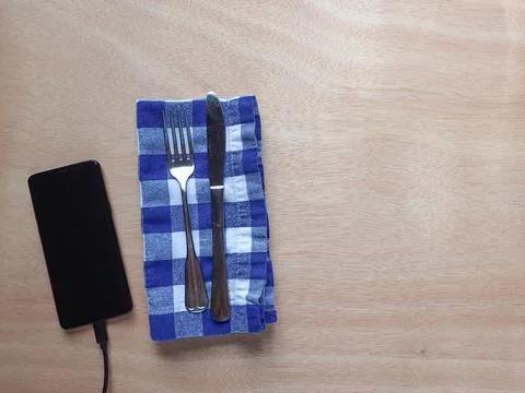 Fork and kinife table setting on a blue and white gingham napkin with a cellp Stock Photos