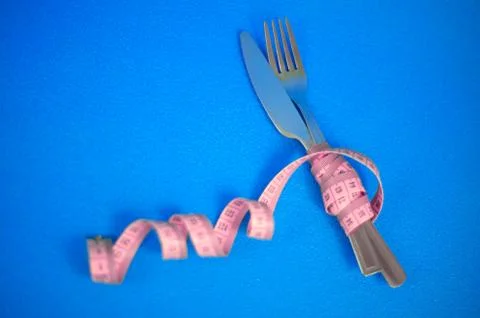 The fork and knife are wrapped in pink measuring tape on a blue background. Stock Photos