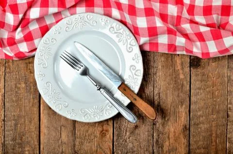 Fork and knife in empty decorative plate and red checkered tablecloth on top Foto stock