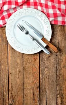 Fork and knife in empty decorative plate and red checkered tablecloth on top Stock Photos
