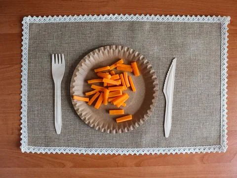 Fork and knife placed beside paper plate of cheese sticks on a brown table Stock Photos