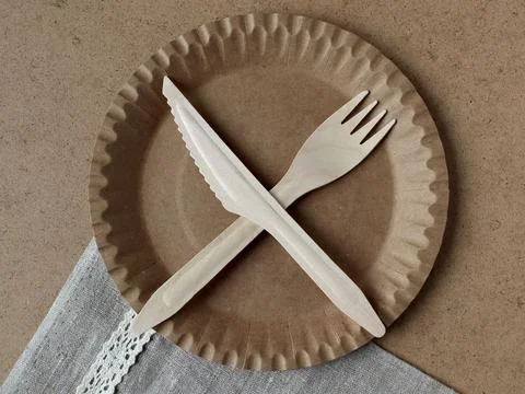 Fork and knife placed on a brown paper plate on a gray cloth background showing Фото
