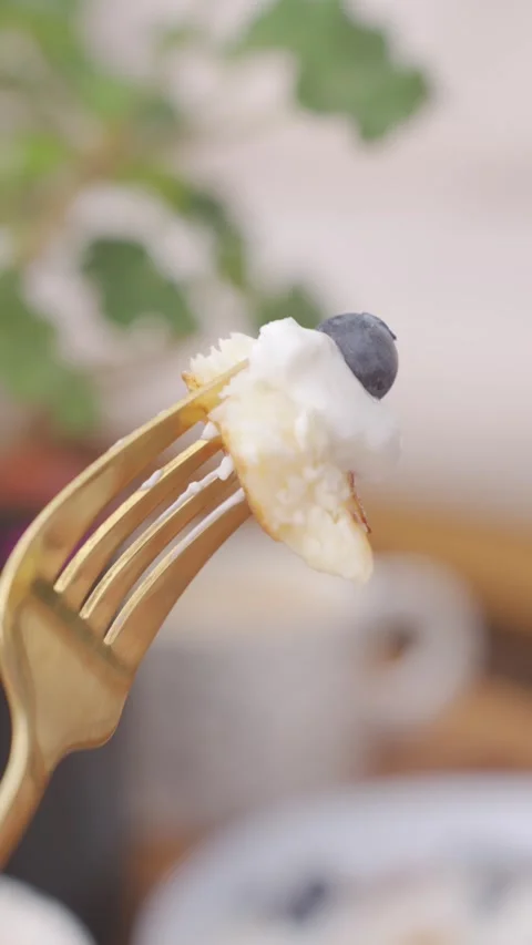 Fork with bite of sweet fried pastry topped with white cream and blueberry Stock Footage 337000397