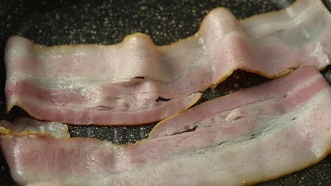 Fork corrects a slice of bacon on the hot surface of the grill. Stock Footage 125931819