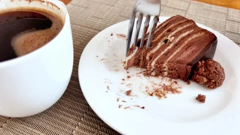 Fork Cutting Layered Chocolate Cake Next to White Coffee Cup on Table Stock Footage 346177455