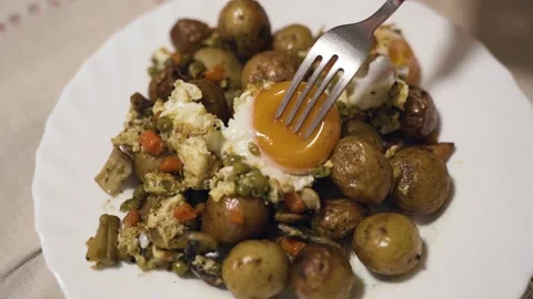 The fork destroys the egg yolk. Potato And fried egg and vegetables. Close up Stock Footage 215948752