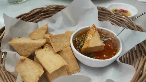 Fork dipping crispy fried tofu into spicy sauce in a basket Stock Footage 336231098