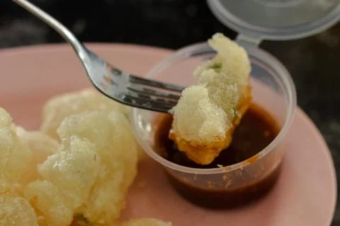 Fork dipping fried Cireng tapioca snack into sweet spicy brown sauce in close Stock Photos