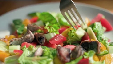 The fork gently stirs a fresh salad of greens, bell peppers, cucumbers and tuna. Video stock 234021438