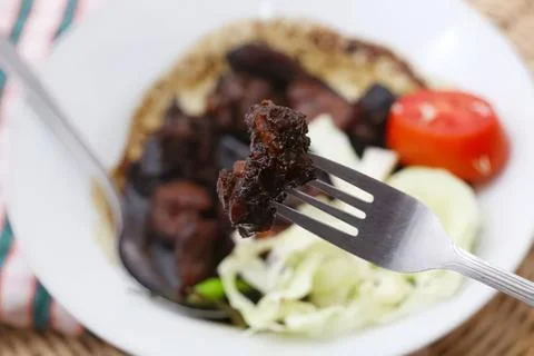 Fork holding cooked beef with vegetables on plate Stock Photos