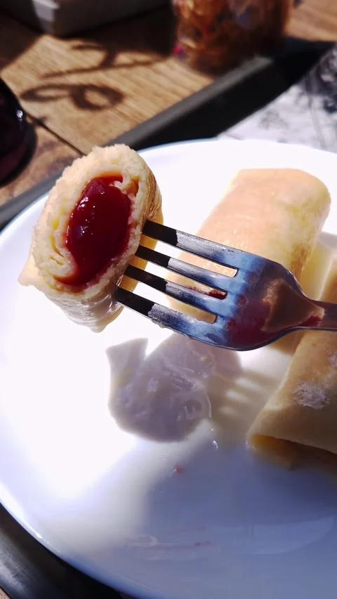 Fork Holding Rolled Crepe with Red Jam Over White Plate on Wooden Table Stock Footage 339084237