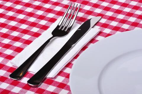 Fork, knife and plate on a table with a red and white tablecloth Stock Photos