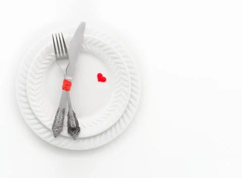 Fork, knife and two red hearts on white plate. Invitation for a romantic dinner Stock Photos