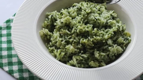 Fork lifting spinach rice from white plate on green checkered cloth in bright Stock Footage 310786178