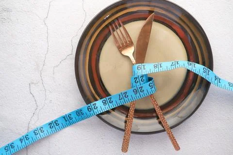 Fork with measurement tape and empty plate on wooden background Stock Photos