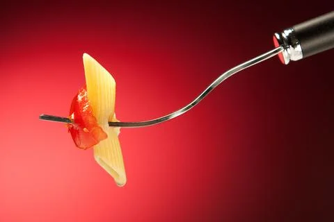 Fork with pasta and tomato on a red background Stock Photos