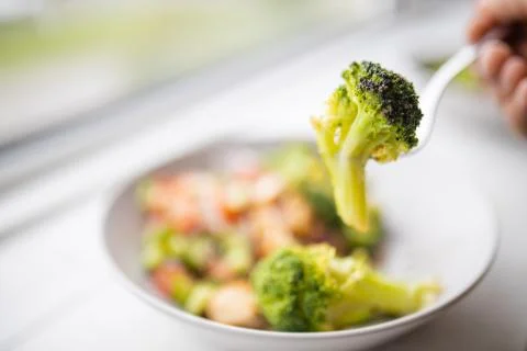 Fork picking broccoli from a broccoli and chicken salad next to a window Stock Photos