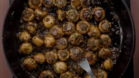 A fork pierces a stewed champignon on a frying pan Stock Footage 296691775