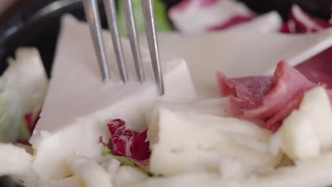 Fork piercing slice of white cheese on fresh salad with radicchio and ham. Stock Footage 332887402