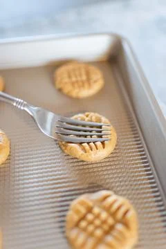 A fork pressing down peanut butter cookies on a baking sheet 스톡 사진