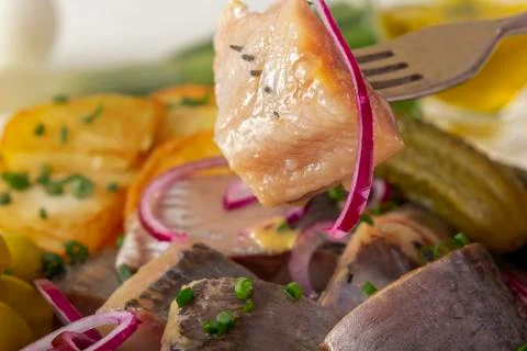 Fork pricks a piece of pickled herring from a plate of fish appetizer, herbs Stock Photos