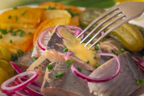 Fork pricks a piece of pickled herring from a plate of fish appetizer Stock Photos