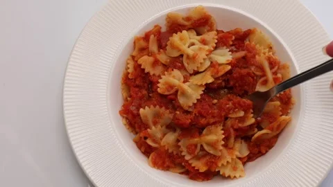 Fork scooping up bowtie pasta in thick tomato sauce, served on elegant whit.. Stock Footage 318903599