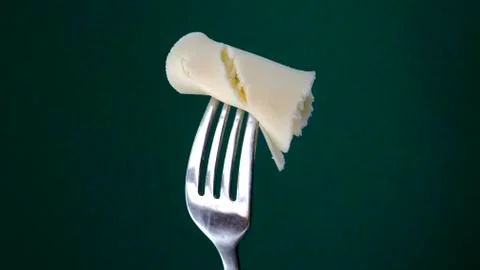 Fork with slice of cheese on green background. Stock Photos
