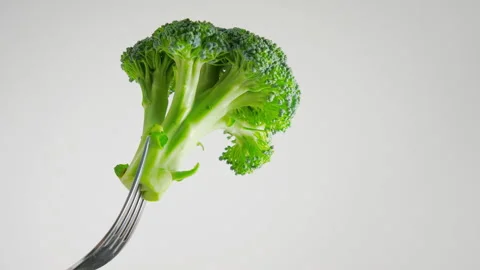 Fork is slowly lifting a floret of fresh, green broccoli on a white background. Video stock 290464407