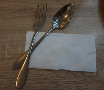 Fork with spoon and tissue paper on a wooden table in a cafe. Stock Photos