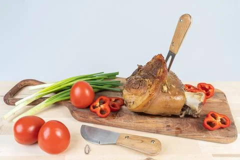 A fork stuck in a pork knuckle and a knife next to it on a cutting board, mea Stock Photos