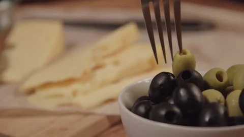 A fork takes an olive from the plate, next on the table is cheese Stock Footage 73919579