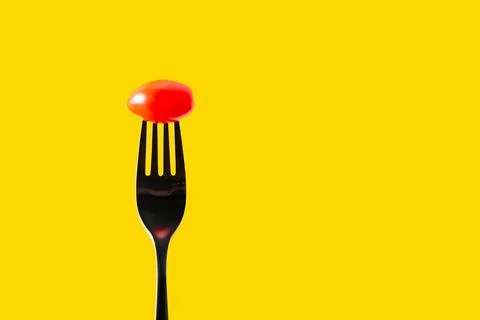 Fork with tomato on yellow background, copy space for text Stock Photos