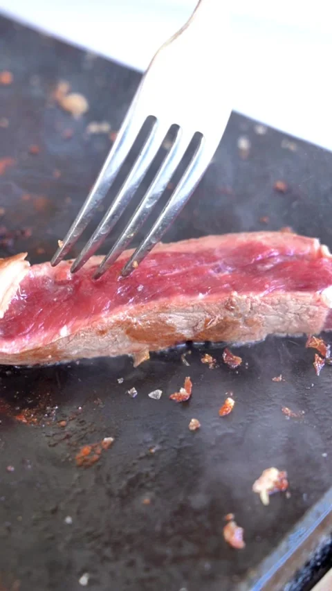 A fork is used to cut a piece of meat. The meat is on a black surface and has Stock Footage 327529297