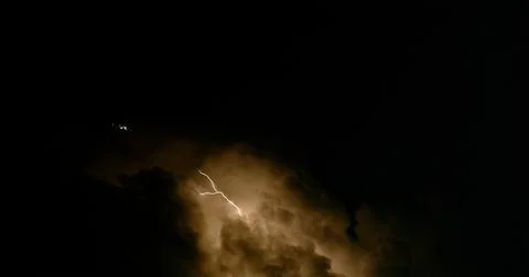 Forked lightning lights up the night sky as a jetliner avoids a thunderstorm. Stock Photos