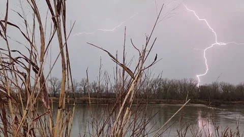 Forked lightning strike over calm river during thunderstorm in winter landscape Stock Footage 330923220
