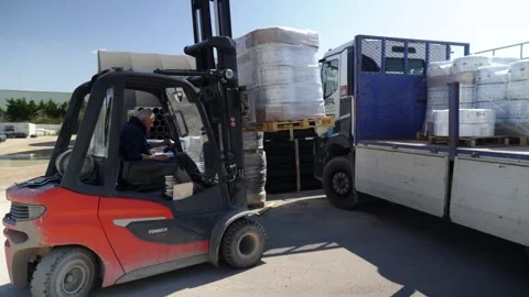 Forklift loading pallets onto a truck in an industrial warehouse yard. Operator Stock Footage 340992154
