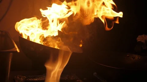 Forks of fire playing on a frying pan kept by chef at outdoor kitchen in slo-mo Stock Footage 112657310