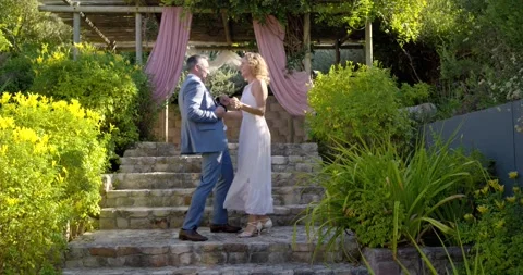 Formal couple descending stone steps at pergola celebrating dancing holding dark Stock Footage 337400614