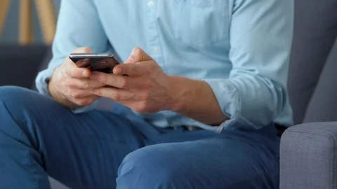 Formally dressed man sits on a sofa and using smartphone for texting message Stock Footage 123458483