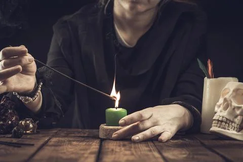 A fortune teller or oracle with objects for fortune-telling lights a candle f Stock Photos