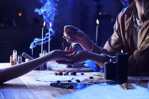 Fortune teller with pendulum reading woman's palm at table Stock-Fotos