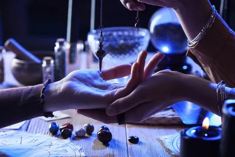 Fortune teller with pendulum reading woman's palm at table, closeup Stock Photos