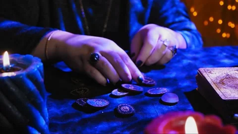 A fortune-teller at a table in candlelight reads the future from runes on black  Stock Footage 237468568